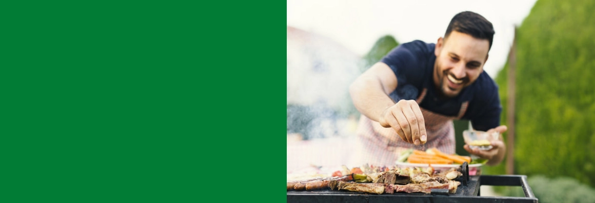Lachende Person würzt das Fleisch auf dem Grill.